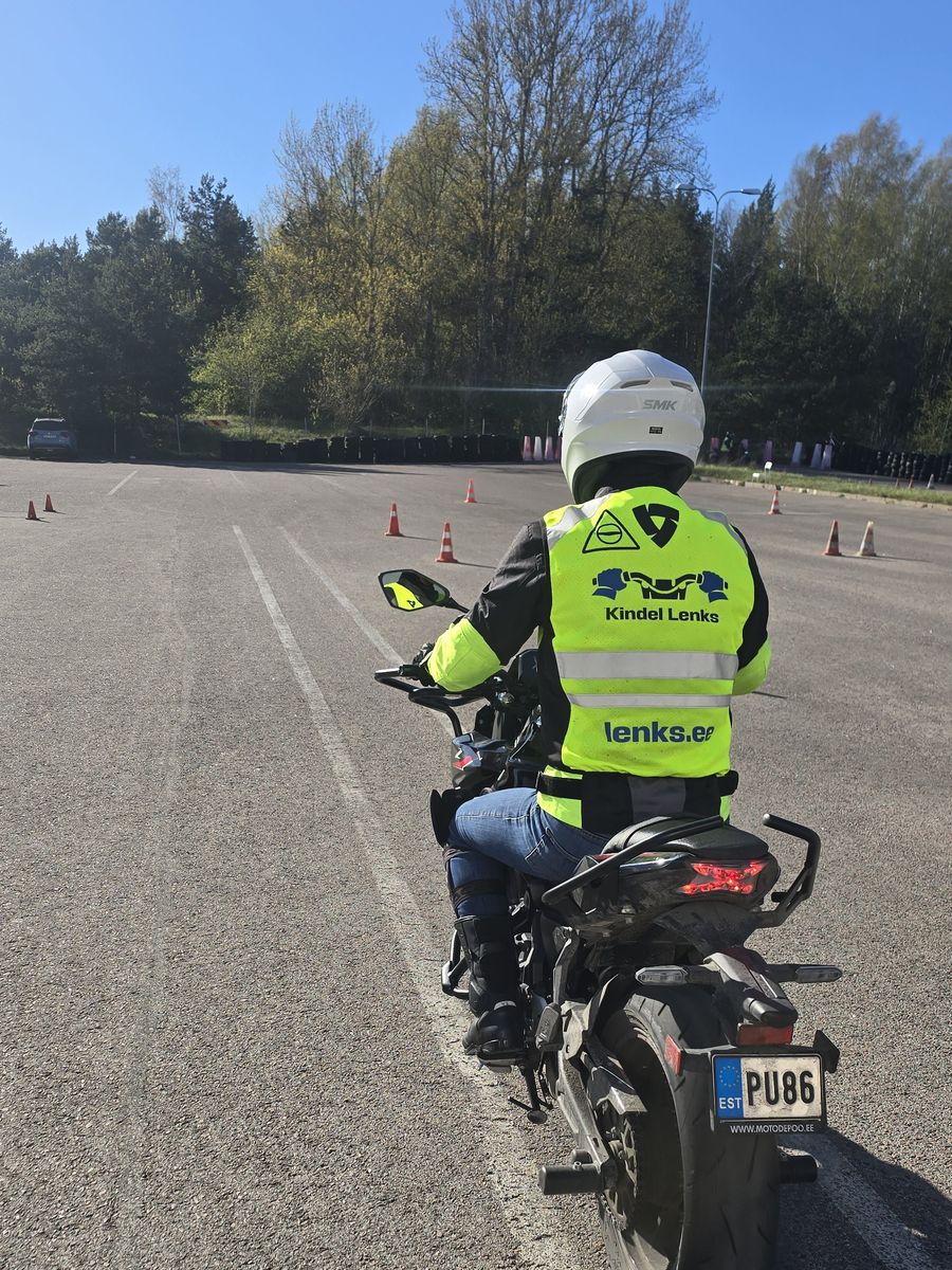 A student on a motorcycle on the training ground on a sunny spring day, wearing a Kindel Lenks motorcycle school vest, cones ahead